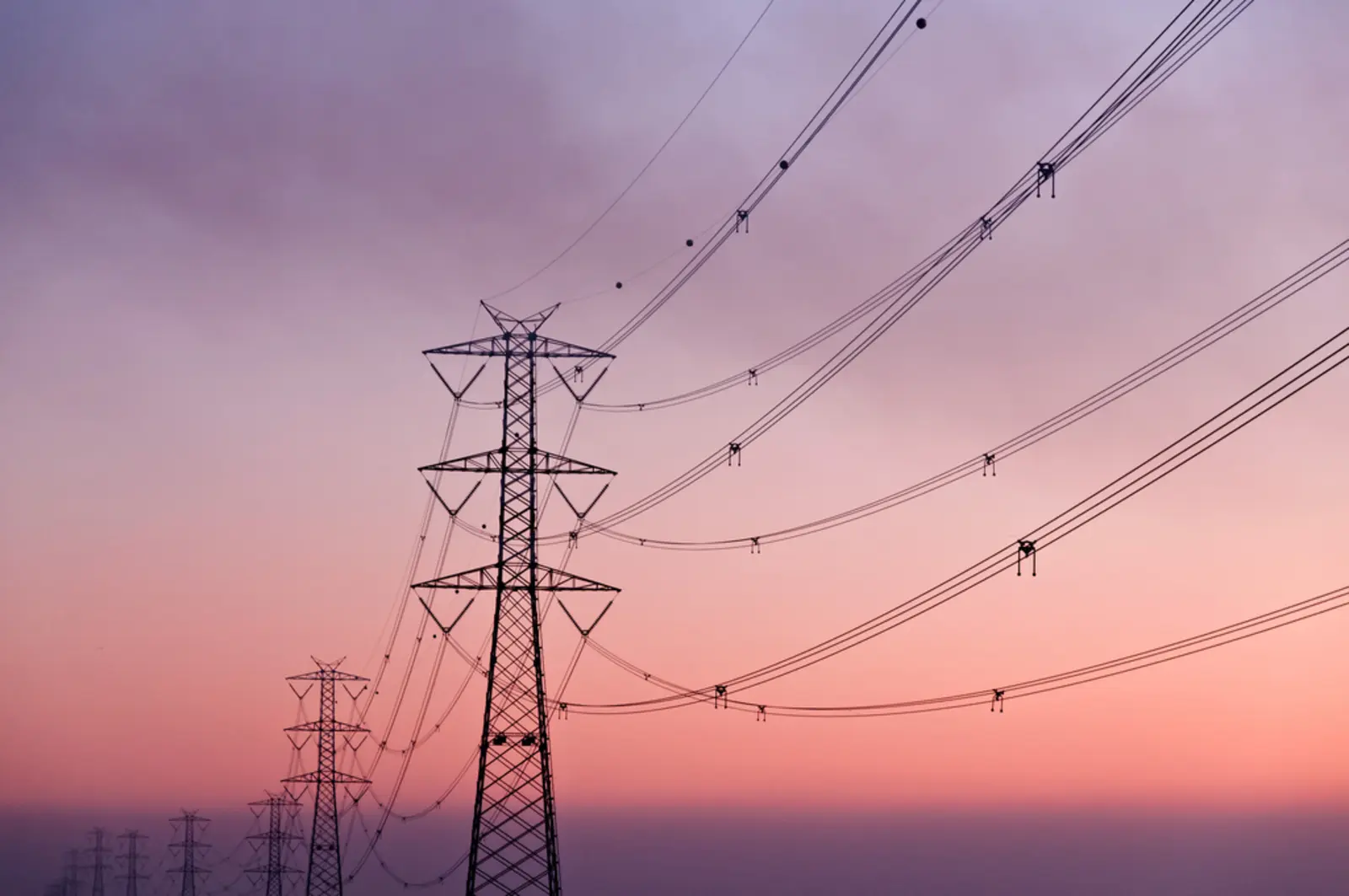 A row of metal electrical transmission towers and sagging power lines recedes into the distance against a gradient pink and purple sky at dusk. The photographer titled it “Diminishing Perspective”.