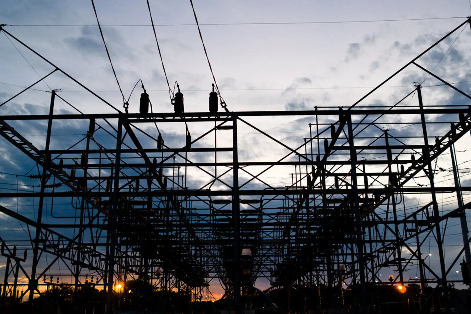 A silhouetted electrical substation featuring metal lattice frameworks and overhead power lines stands against a cloudy twilight sky. The photographer titled it “Dusk II”.