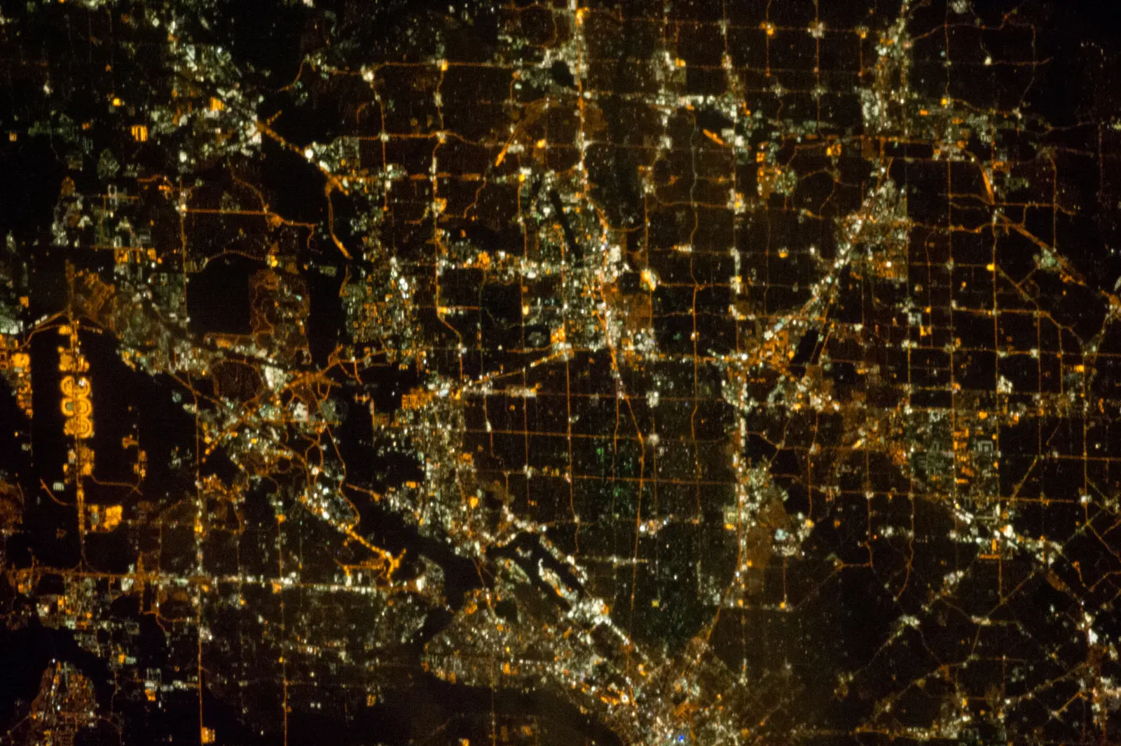 A nighttime view from orbit shows a sprawling city rendered as a dense grid of orange and white streetlights and bright clusters of development, broken by dark patches of unlit land. The photographer titled it “Earth Observation taken by the Expedition 33 crew”.