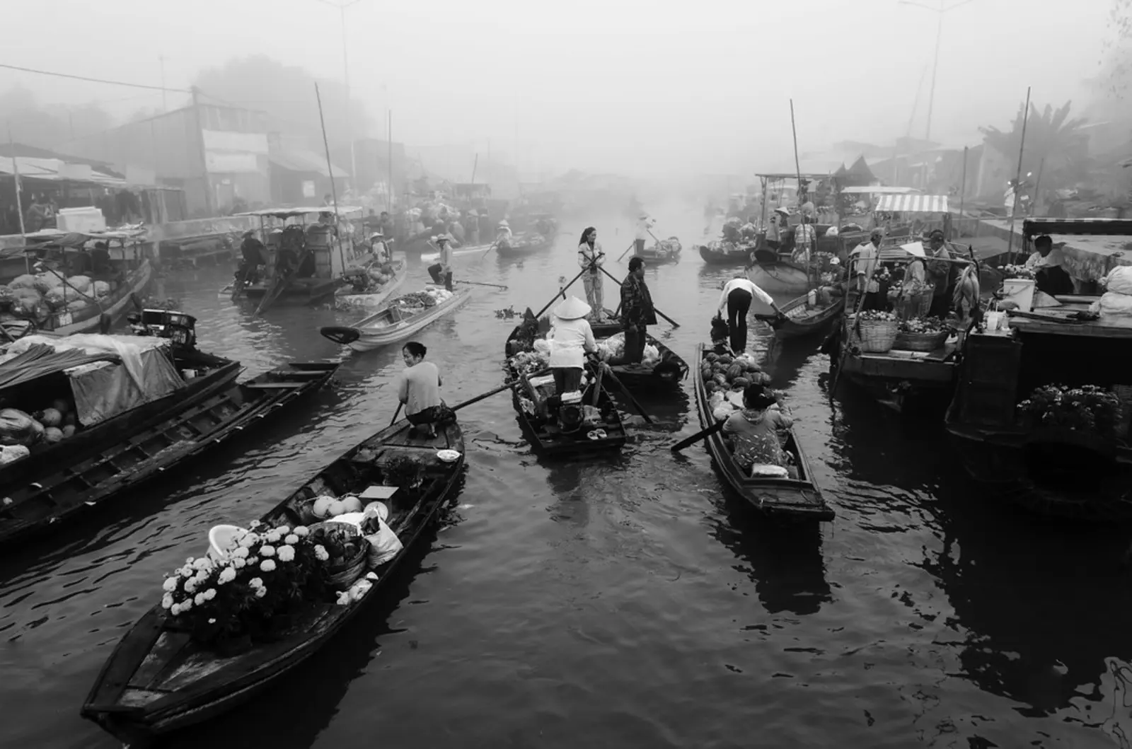 Several small wooden boats carrying goods and passengers navigate a foggy river. The photographer titled it “floating market. Nganam town, Soctrang province, Vietnam. Jan 26th. 2014”.