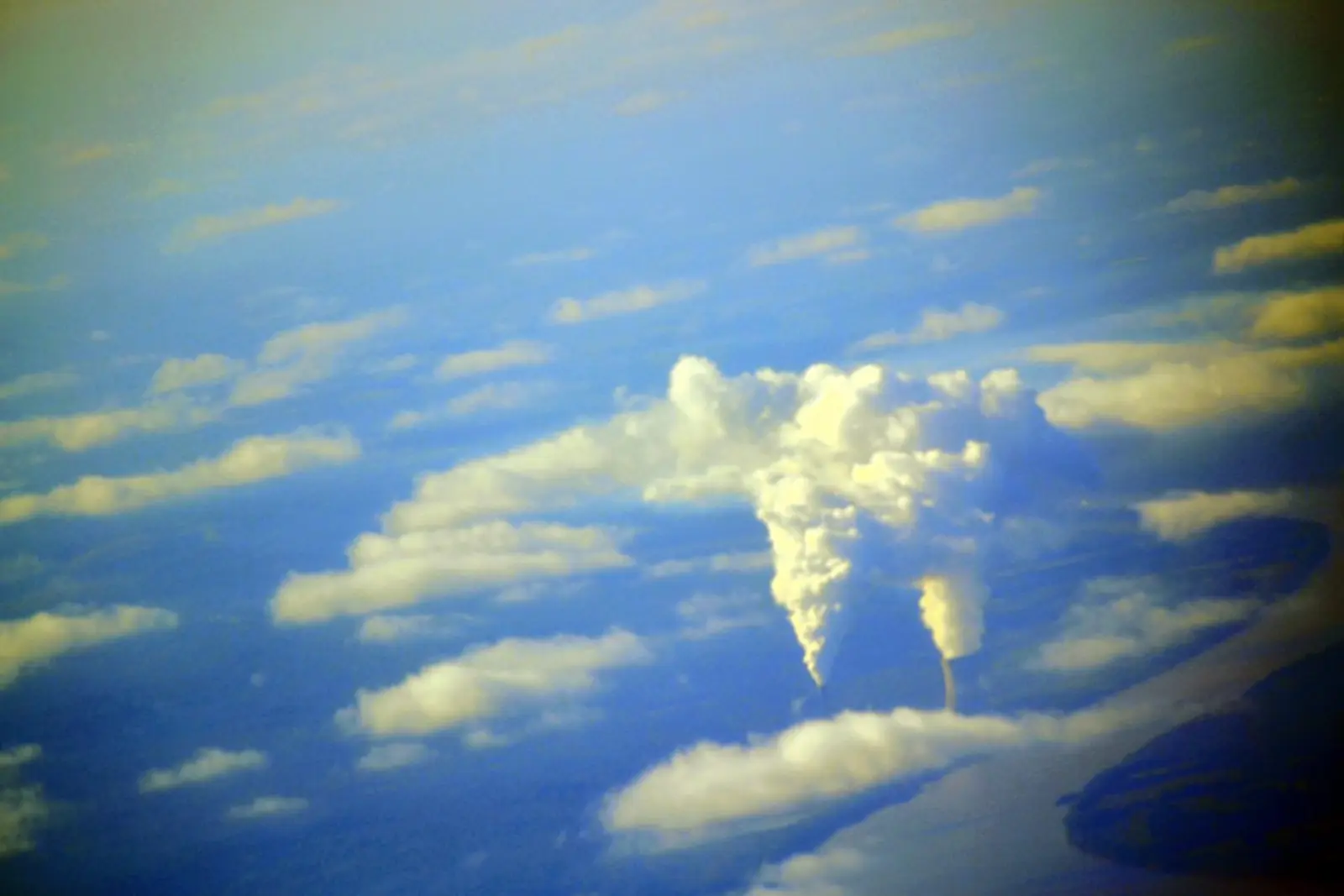 Two industrial cooling towers release thick plumes of white vapor into a blue sky with scattered clouds.