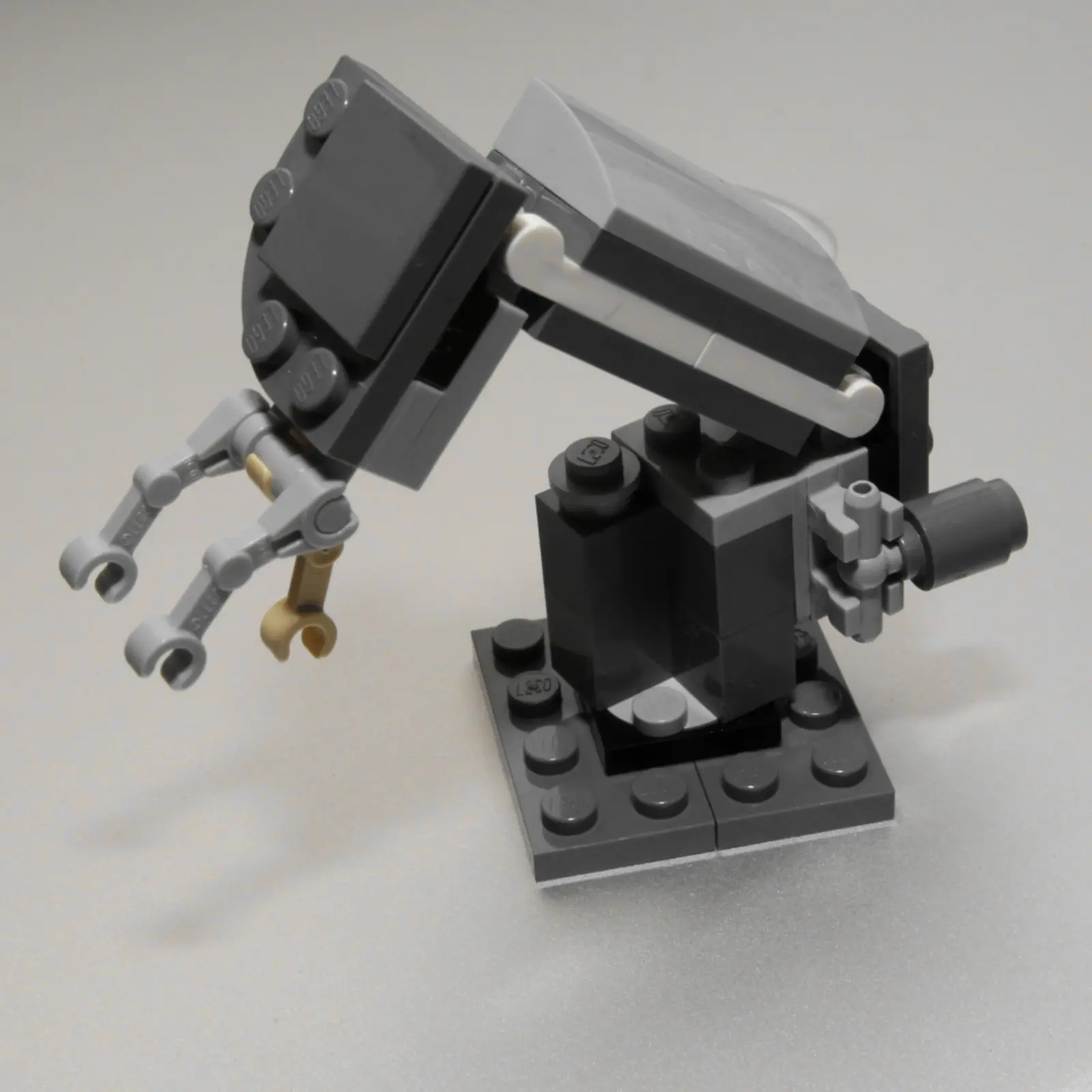 A small robotic arm constructed from gray, black, and tan plastic building blocks is shown against a plain background. The photographer titled it “Robot Arm”.